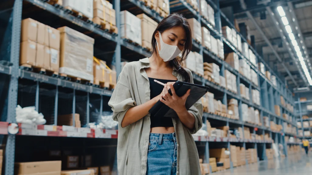 Een medewerkster met mondkapje in een distributiecentrum controleert de voorraad op een tablet