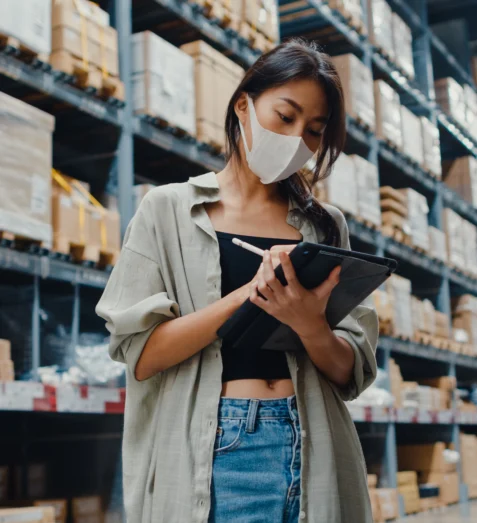 Een medewerkster met mondkapje in een distributiecentrum controleert de voorraad op een tablet